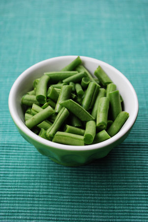 Fresh raw green beans in a ceramic bowl on green fabric gackgroundの写真素材