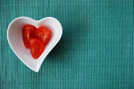 Red tomatoes salad in heart shape bowl on green backgroundの写真素材