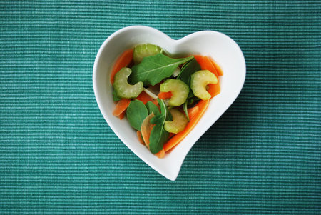 Various vegetables salad in heart shape bowl on green backgroundの写真素材