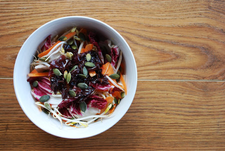 Red salad with carrots, sprouts, pumpkin seeds and seaweed in white bowl on wooden の写真素材