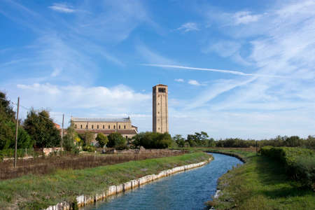 Ancient medieval bell tower of Santa Maria Assunta Cathedral with canal, in the Island of Torcello near Veniceの写真素材