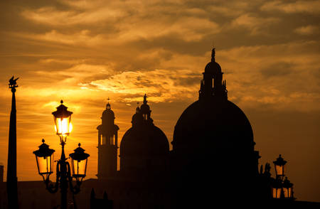 Venice sunset with Salute Basilica (Saint Mary of Health) baroque domes, lamp and Saint Mark Lion silhouetteの写真素材
