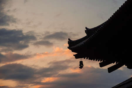 Buddhist temple roof with ancient bell toward sunsetの写真素材