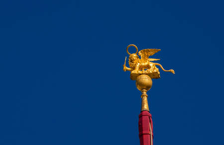 Saint Mark Winged Lion golden statuette wielding a sword against blue sky, a symbol of the Old Venice Republic at war (with copy space)の写真素材