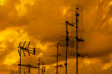 Different kinds of TV antennas and arrays with golden sunset sky and clouds