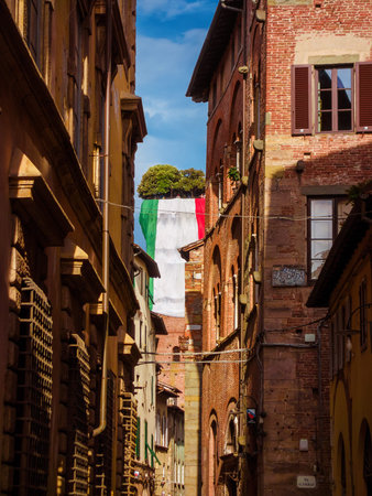 LUCCA, ITALY - MAY 22, 2025: Guinigi Tower with Italian National Flag seen from medieval narrow street in the city centerのeditorial素材