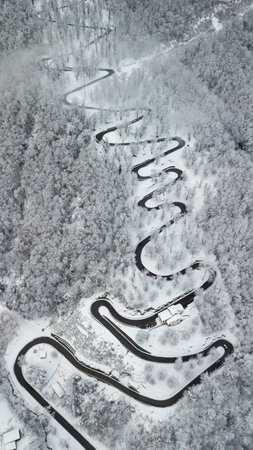 mountain road with many curves through snowy forest in switzerland