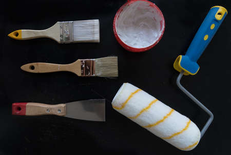 Kit of two paint brushes, roller paint, spatula and wall putty on black backgroundの写真素材