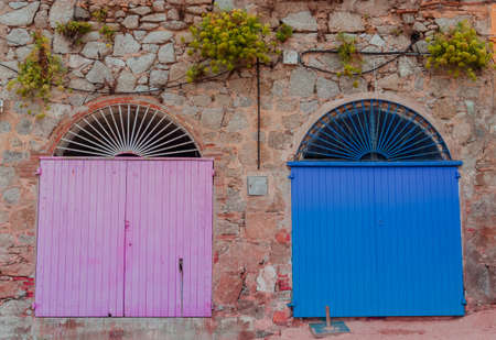 Ancient pink and blue wooden doors on a stone wall in Calella de Palafrugell village.の写真素材