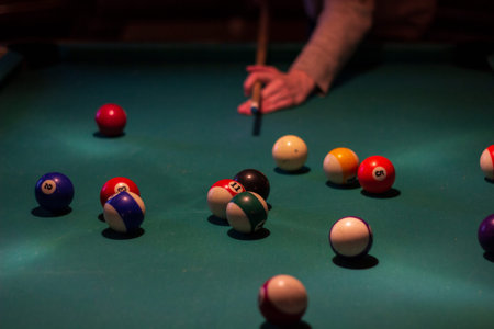 Woman's hand after hitting the billiard cue ball. A lot of billiard balls scattered on the pool