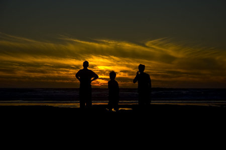 Three young people watching sunset over the sea on coast of Cornwall UKの写真素材