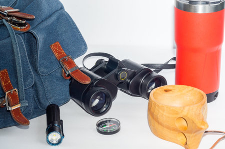 Backpack, compass, binoculars and flashlight, camping mug and thermos-a hiking kit.