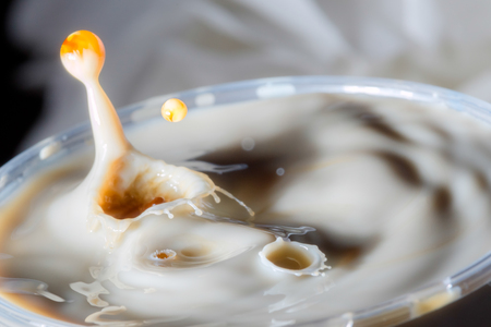 high speed photograph of a caramel milk drop on dark background in the studioの写真素材