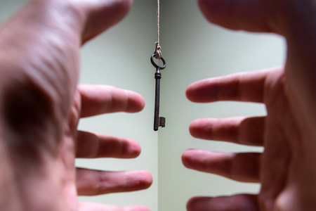People hands reaching for vintage key hanging on a string. Business success freedom concept concept for aspirations, achievement and incentiveの写真素材