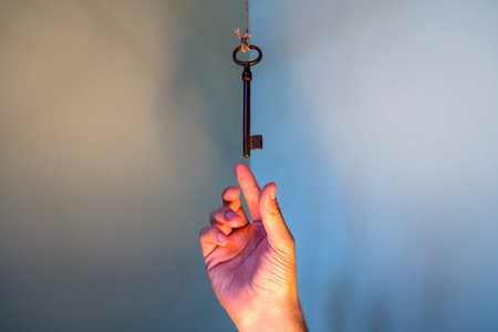 People hand reaching for vintage key hanging on a string. Business success freedom concept concept...
