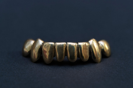 Golden teeth grillz on black background. Street culture gold jewelry accessoriesの写真素材