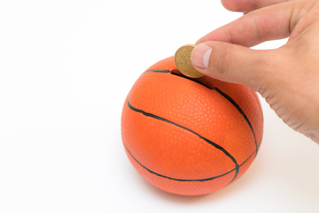 Male hand putting euro coin into the piggy bank with a shape of basket ball isolated on white backgroundの写真素材