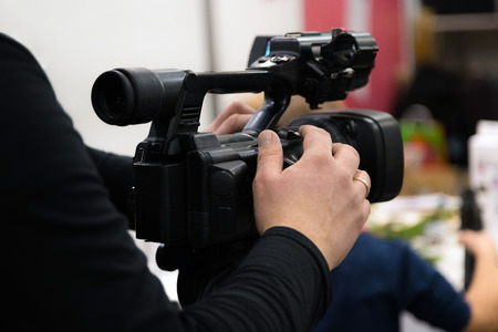 Covering an event with a video camera. Videographer films with video camera. Camera operator working indoorsの写真素材