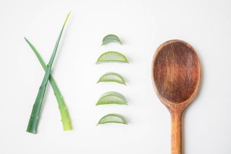 Aloe vera twigs and plant slices on white background with wooden spoon on the sideの写真素材