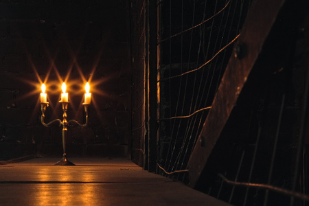 Group of evil candles burning in the darkness and copy space on wooden background with metal fence on the side. Black magic ritual or scary halloween rite.の写真素材