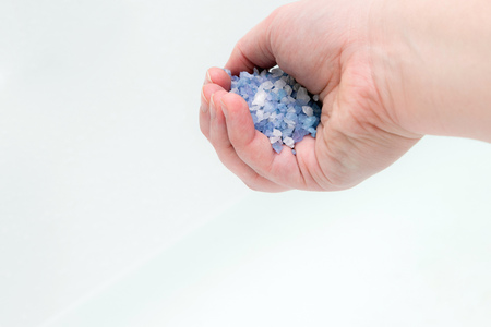 Close up of woman's hand poring bath salt crystals into water. Spa treatment, relaxationの写真素材