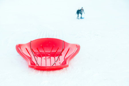 Red plastic sleigh, sledge, sled on white snowy background outdoors. Winter play and activity for...