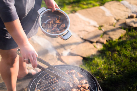 Woman hands grilling barbeque meet on the grill outdoors in the back yard. Summer time picnic. Roasting meat on metal grid on hot coals. Smoke adds a smoky flavorの写真素材