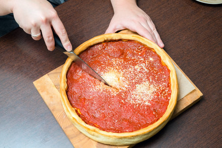 Top view of Chicago pizza. Woman hands cutting Chicago style deep dish italian cheese pizza with tomato sauce and beef meet insideの写真素材
