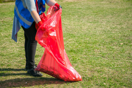 Woman volunteer wearing picking up trash and plastic waste in public park. Young girl wearing gloves...