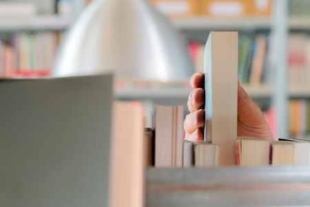 Young student picking a book from the shelf in the library. Preparing for exams, young man searching for or choosing a book in the public library in universityの写真素材