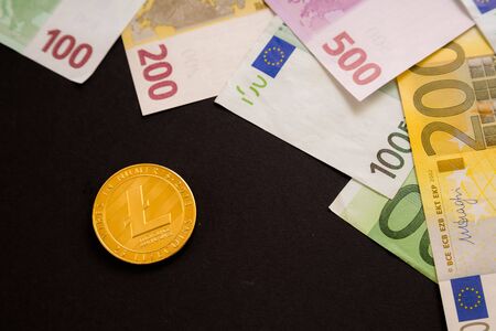 Litecoin coin next to Euro bank notes on black background. Digital currency, block chain market. Euro bills next to crypto coinの写真素材