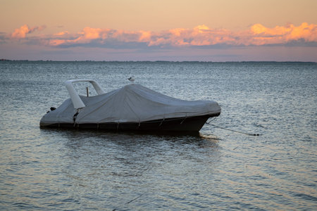 Covered boat docked at the pier by the shore at sunset. Covered yacht on the water with colourful...