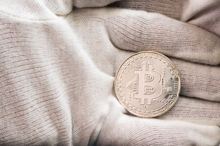 Man in white cloves holding Bitcoin coin between hand palms. Digital currency, block chain marketの写真素材