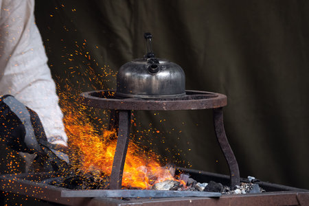 Blacksmith heating up metal in red hot coals while tea pot boiling water on top. Craftsman hand...
