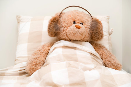 Teddy bear with headphones listening to music in bed. Plush toy in blankets listening to bed time songsの写真素材