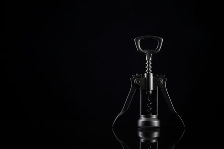Silver colored bottle opener on black background. Universal shiny corkscrew tool with spiral for opening beverage drinks isolated on dark backdrop with space for textの写真素材