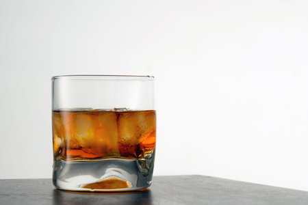 Glass of aged golden whiskey with ice cubes on the table. Amber colored alcohol beverage with rocks...