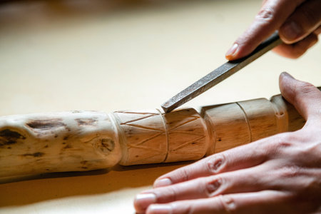 Process of man making wooden walking stick indoors during quarantine. Carving wood stick on the...