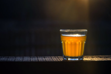 Small glass of craft beer with no foam on a wooden plank outside with space for text. Golden sample...
