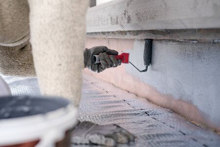 Man painting home socle with paint roller. Close up of rolling grey paint on building plinth. Home renovationの写真素材