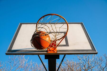 Street basketball ball falling into the hoop. Urban youth game. Close up of orange ball above the hoop net. Concept of success, scoring points and winningの写真素材