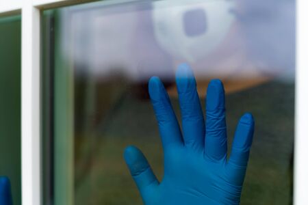Women hand with medical gloves next to the window indoor. Home isolation. Coronavirus. Stay at home.の写真素材