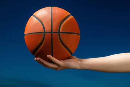 Close up of professional basketball player holding a ball in the hand. Street basketball athlete with a ball and blue sky in the backgroundの写真素材