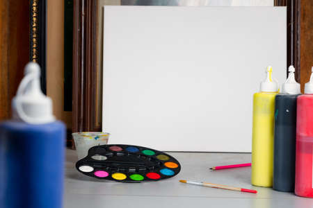 Colorful palette of watercolor paint and brush next to white canvas at artist studio. Creativity and education concept. Nobody, space for textの写真素材