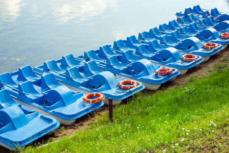Plastic rental pedal boats parked on the lake shore on a sunny day. Active rest outdoors. Nobodyの写真素材