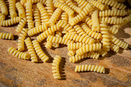 Uncooked curly pasta on wooden table background. Stack of traditional dry raw macaroni. Nobody