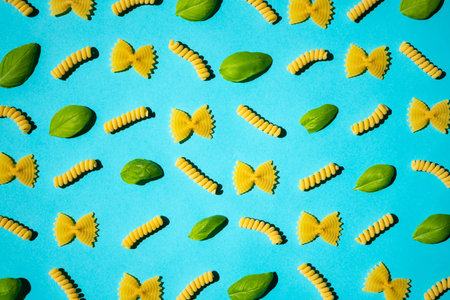 Uncooked curly pasta and basil leaf pattern on blue background. Traditional dry raw macaroni...