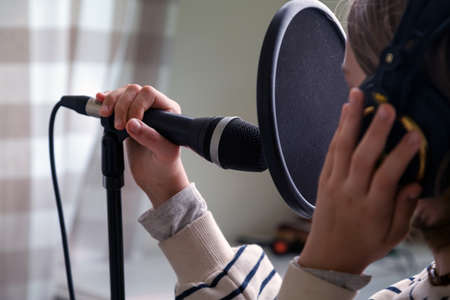 Closeup of teenager recording music in home studio. Girl with headphones and microphone recording songの写真素材