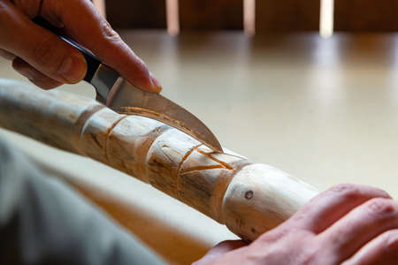 Process of man making wooden walking stick indoors during quarantine. Carving wood stick on the table using knifeの写真素材
