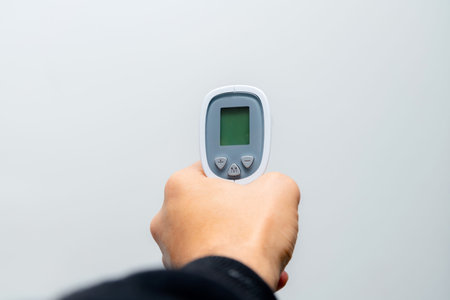 Doctor hand holding temperature gun on grey background. Close up of hand pointing thermometer in a hospital.の写真素材